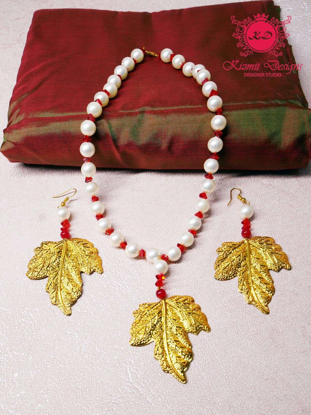 Pearl and red bead necklace with gold leaf pendant and matching earrings, flat lay