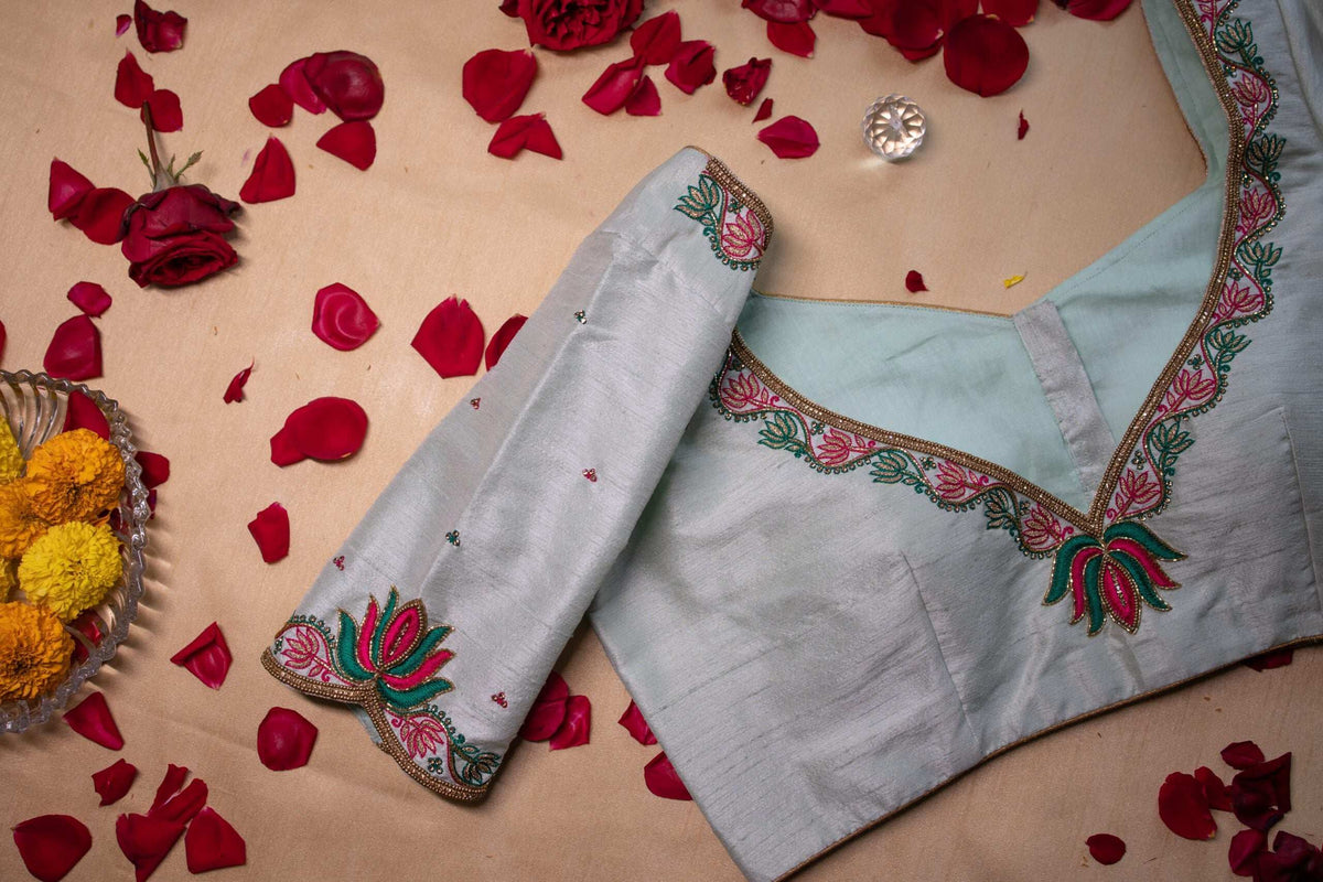 Pale blue blouse folded to show its lotus embroidered neckline, rose petals scattered around
