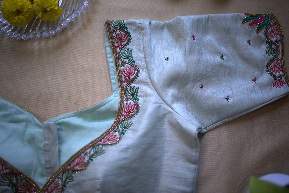 Lotus motif embroidery along the neckline and sleeve hem of the pale blue blouse, close-up