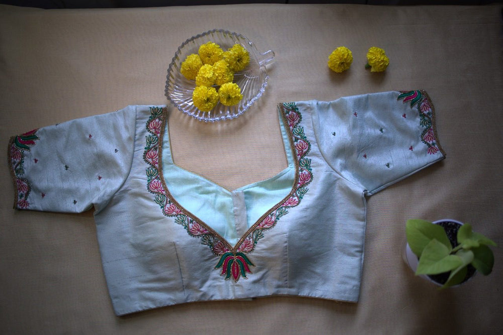 Flat lay of the lotus embroidered blouse with marigolds beside the deep V neckline