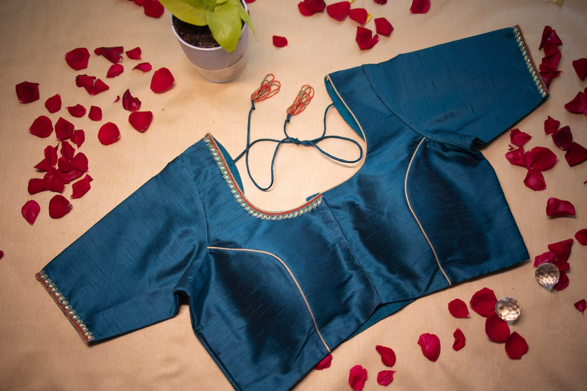 Teal blouse laid flat with pearl-edged neckline and dori ties, rose petals around