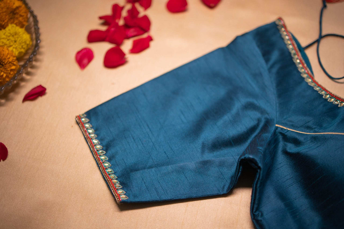 Sleeve hem of the teal blouse edged with pearls and fine gold piping, close-up