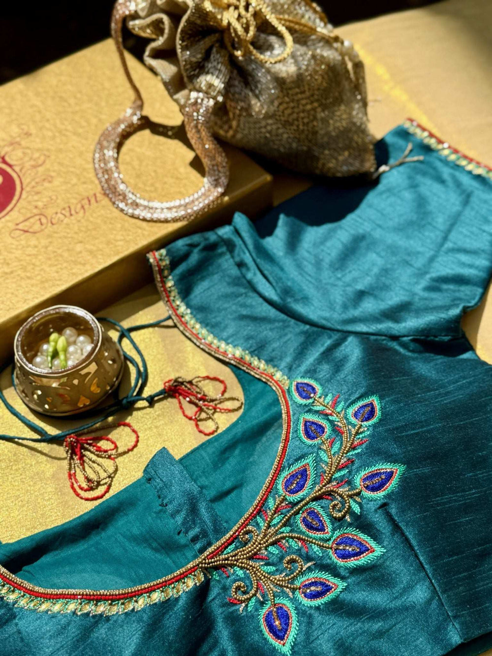 Neckline embroidery of the teal blouse beside a gold potli bag and gift box