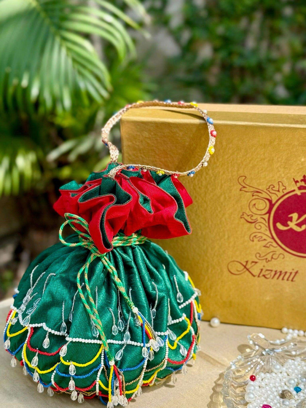 Green potli bag with red gathered top and beaded scallops, set against a gold gift box