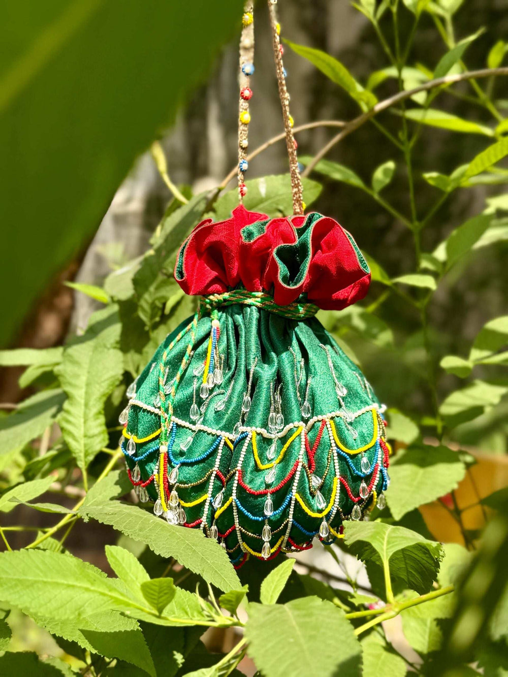 Potli bag hung by its beaded handle among leaves, bead fringe visible all round