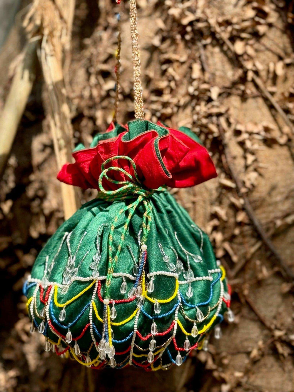 Green potli bag hanging against tree bark, multicoloured bead loops along the base