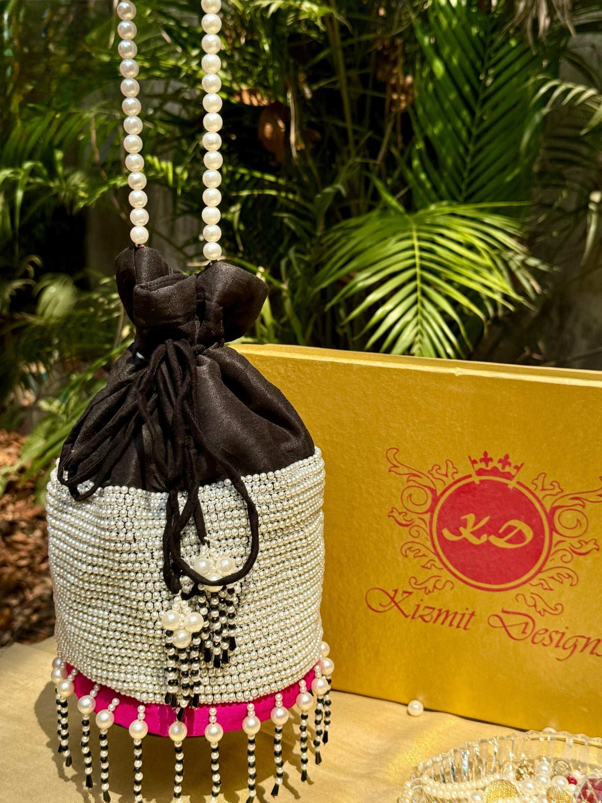 Potli bag hanging by its pearl chain, magenta base band and beaded tassels