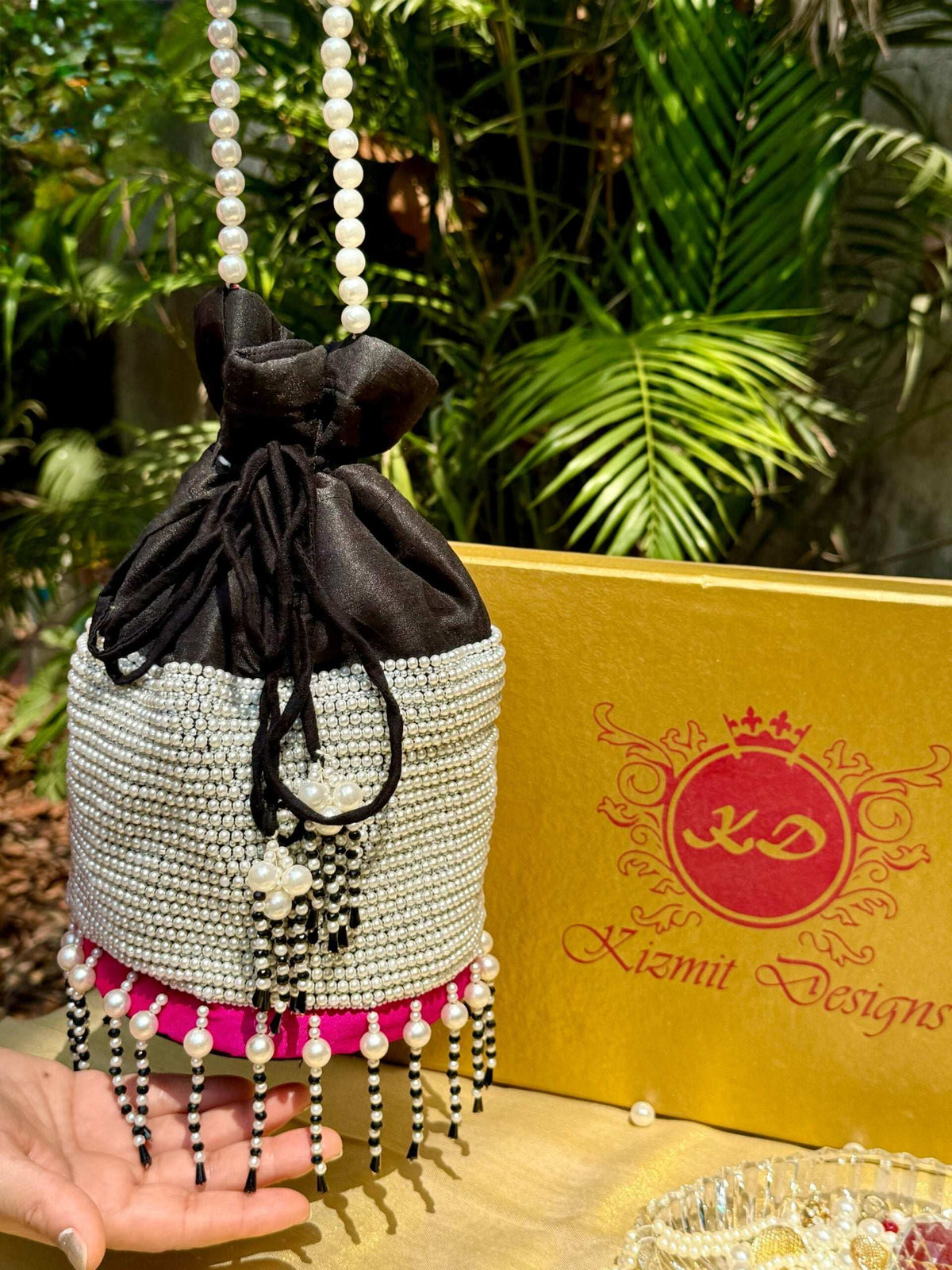Pearl potli held upright, black drawstring gathered at the top, greenery behind
