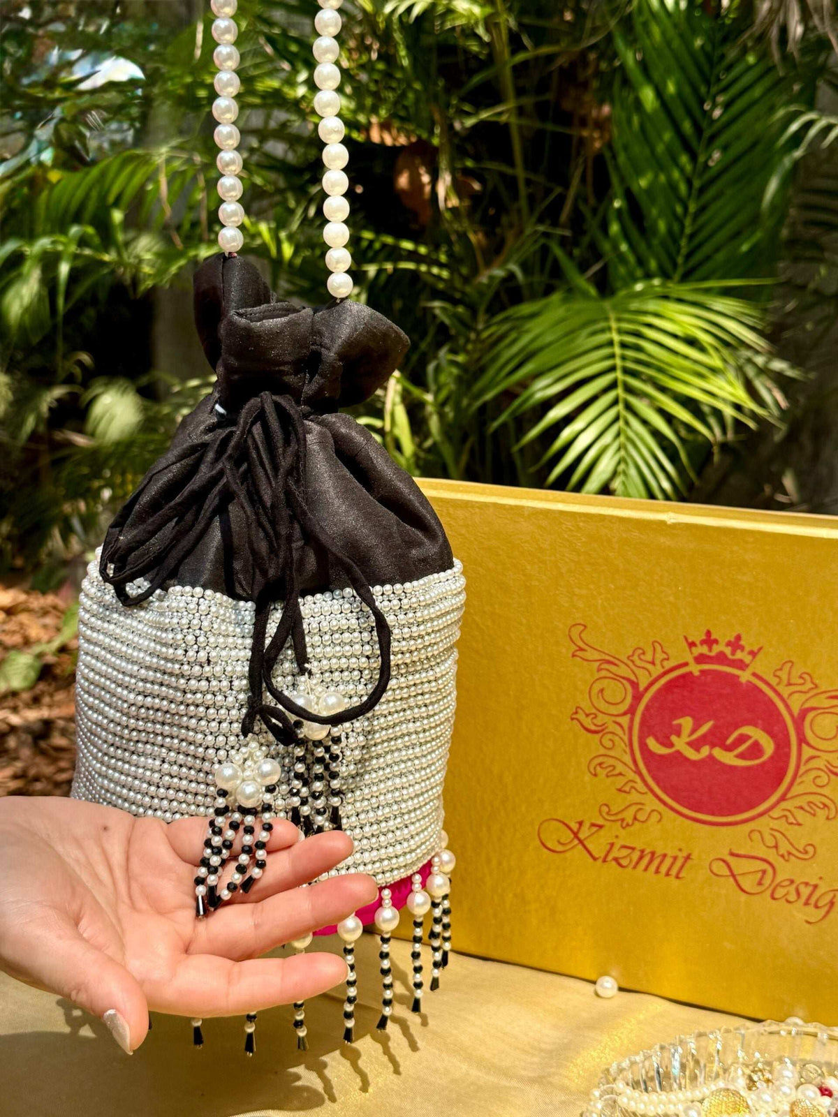 Hand cupping the potli's beaded tassel fringe, showing the bag's size