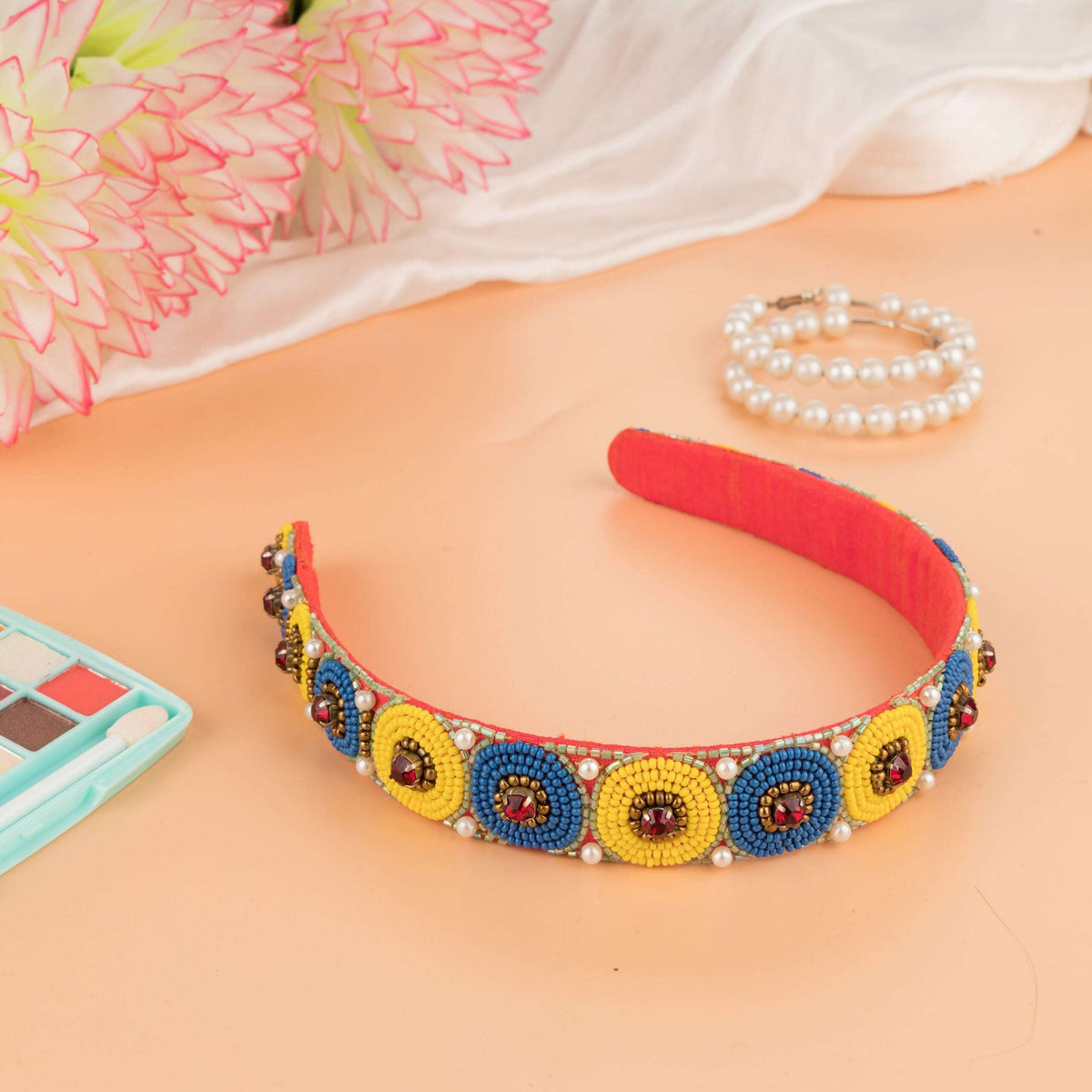 Blue and yellow beaded polka headband on a peach surface with flowers and pearls