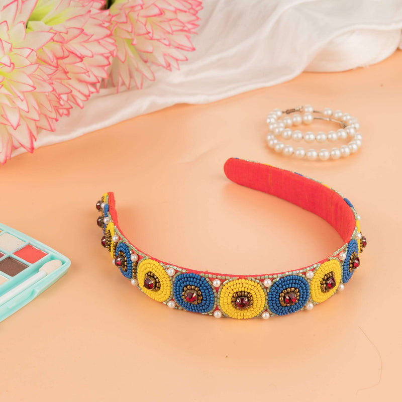 Blue and yellow beaded polka headband on a peach surface with flowers and pearls