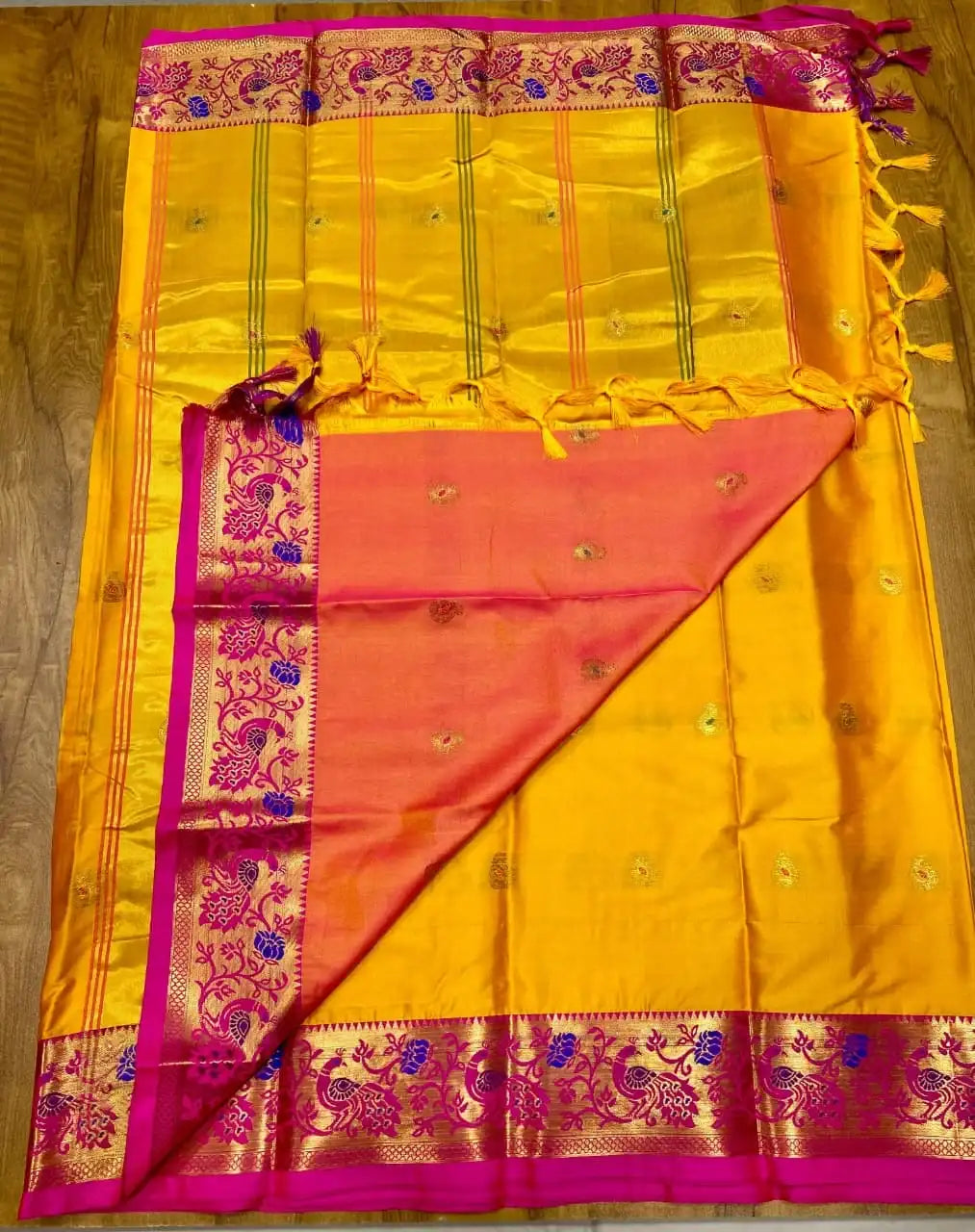Mustard yellow Paithani saree laid out, pink zari border and gold striped pallu with tassels