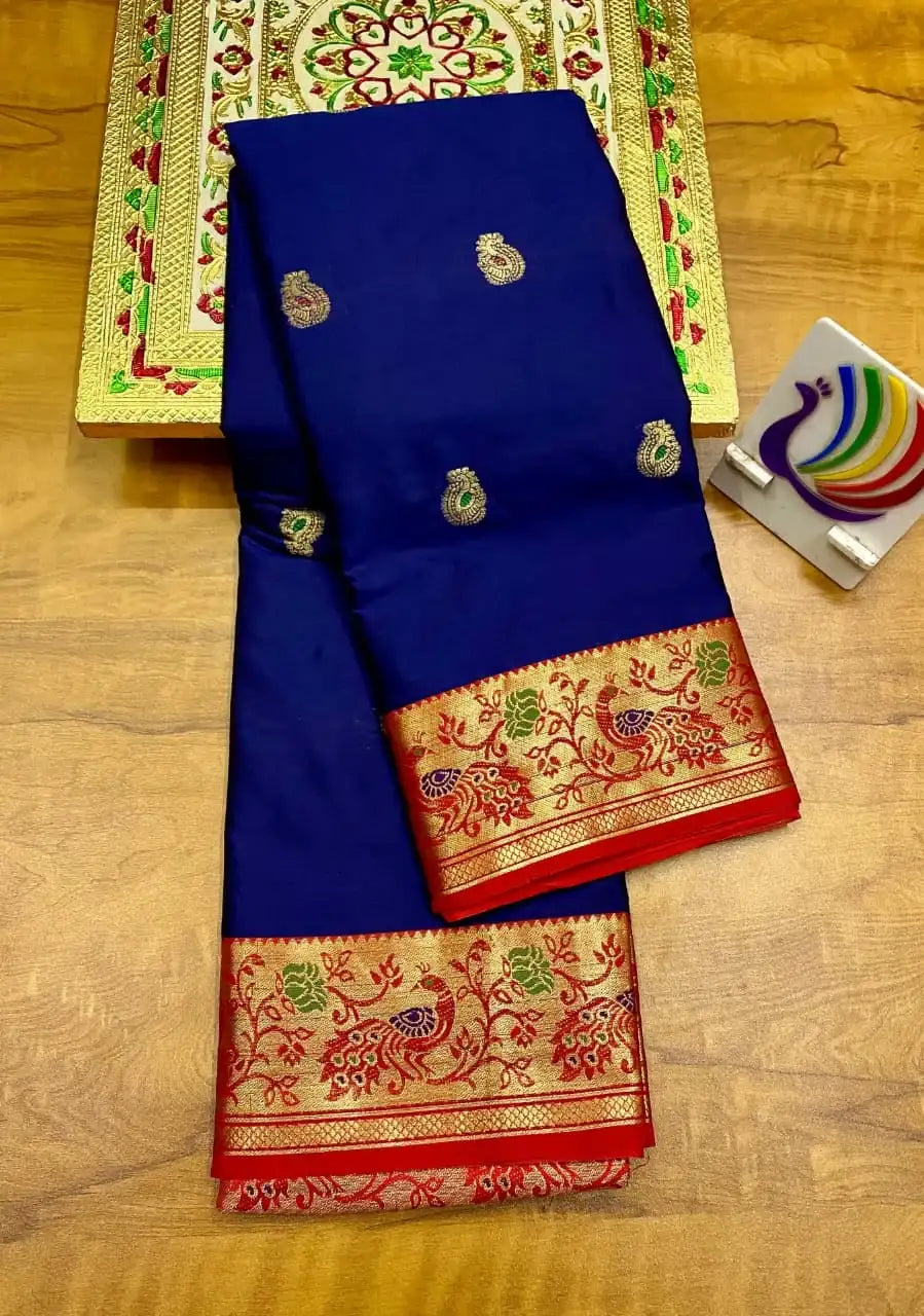 Royal blue saree folded on a wooden floor, red Paithani border with gold peacocks