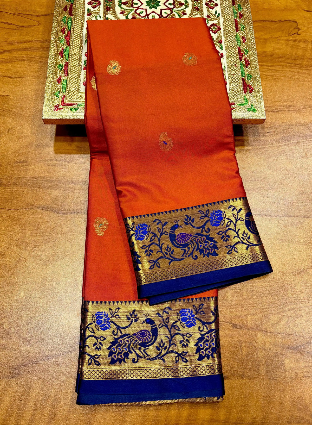 Rust orange Paithani saree folded, royal blue border with gold peacock and flower weave