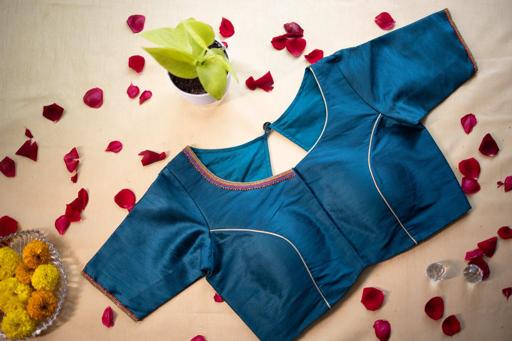 Peacock blue blouse flat-laid among rose petals and marigolds, back view