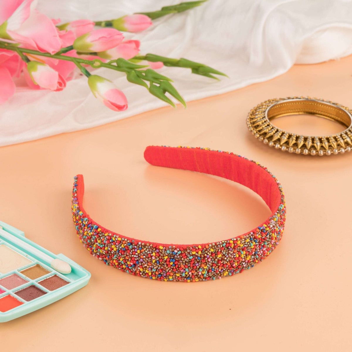 Multicolour beaded headband on a peach flat-lay with pink tulips and an eyeshadow palette