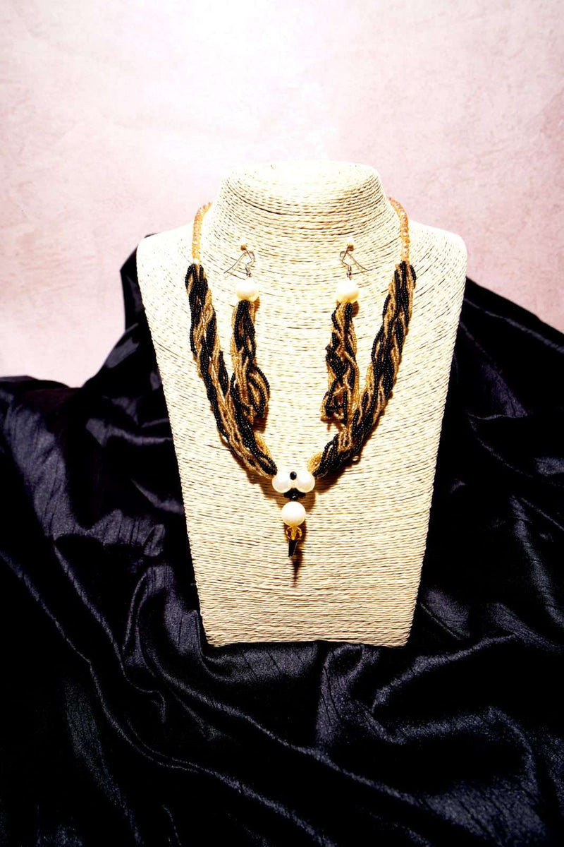 Black and gold twisted bead necklace with matching earrings on a jute bust stand