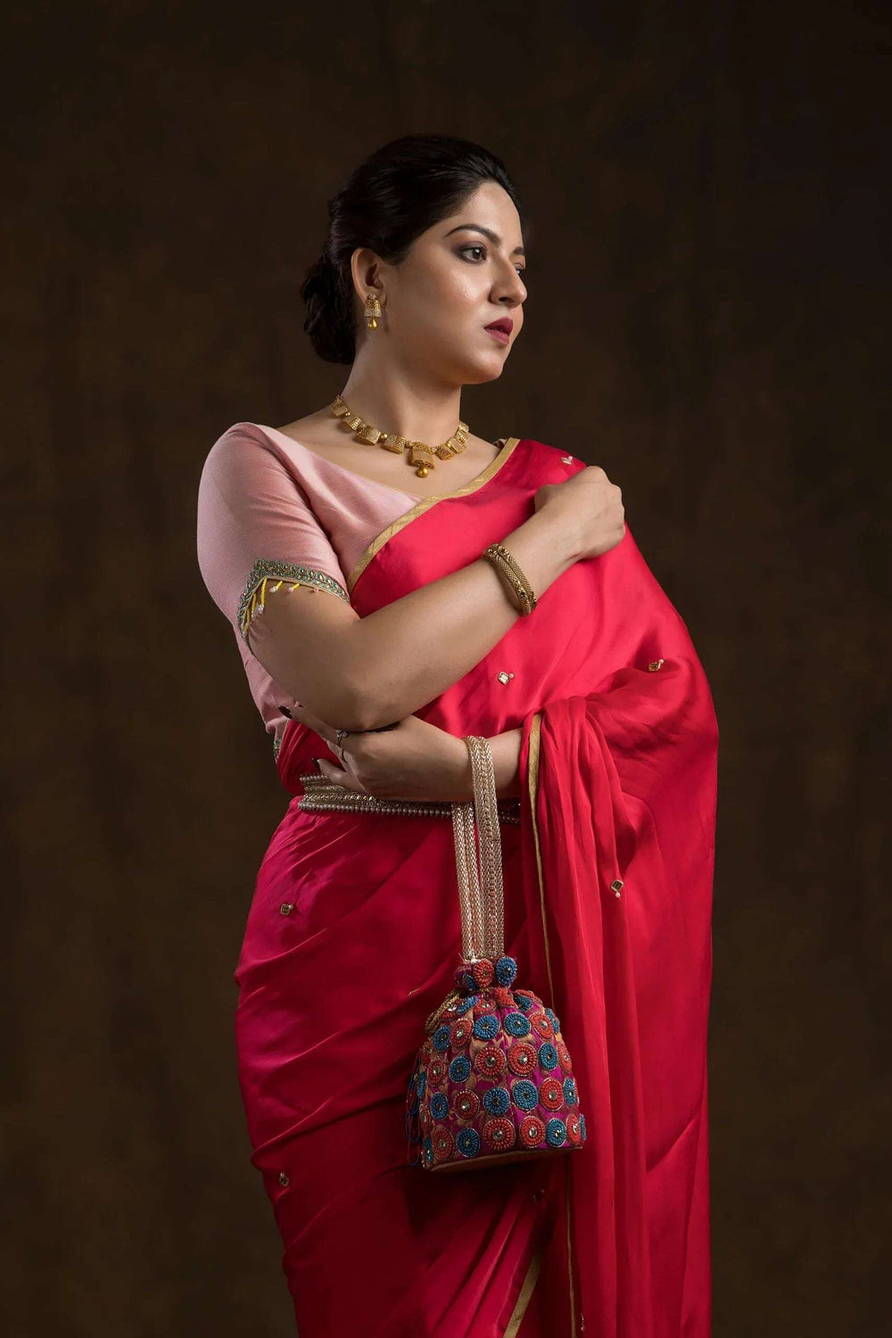 Model in the peach blouse with elbow sleeves, red saree draped over and a floral potli on her arm
