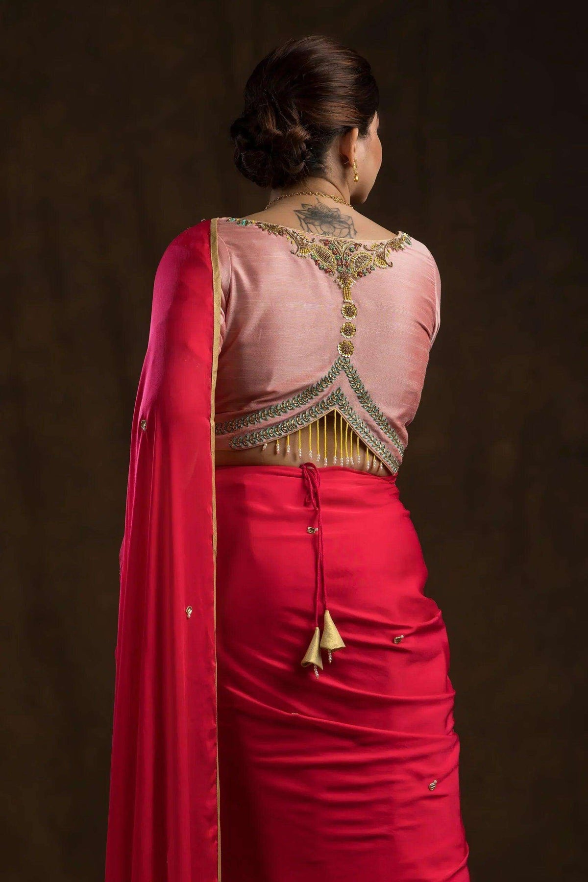 Close back view of the embroidered neckline, gold fringe and dori tassel on the peach blouse