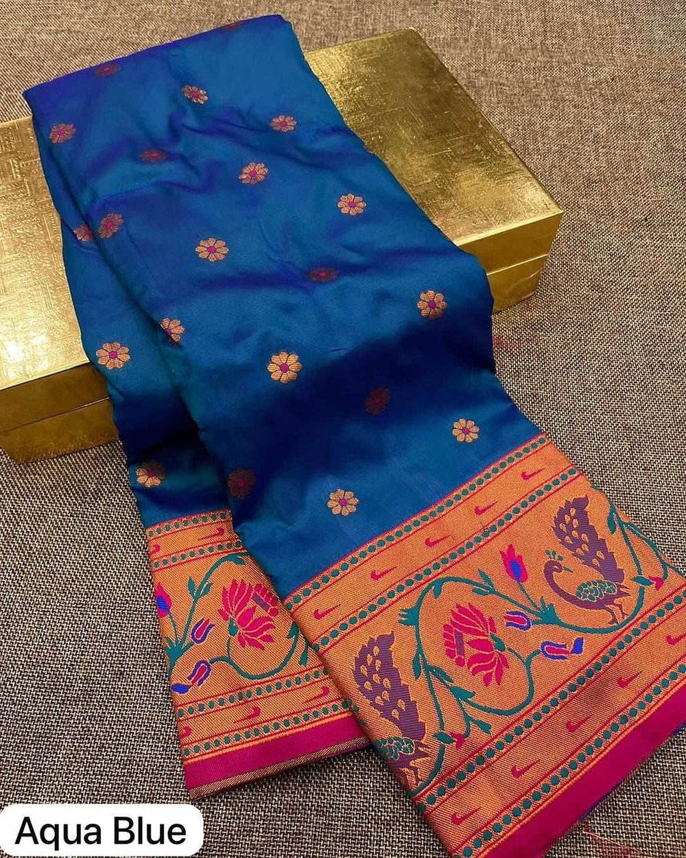 Aqua blue Peacock Lotus Paithani saree folded on a gold box, flower bootis across the body