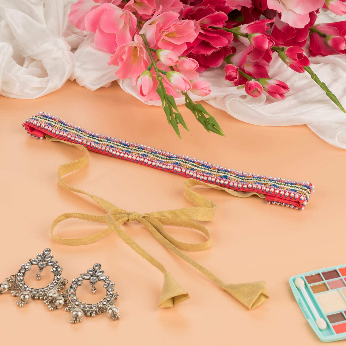Beaded saree belt with gold ribbon ties on a peach surface with pink flowers and oxidised earrings