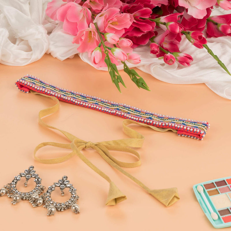 Beaded saree belt with gold ribbon ties on a peach surface with pink flowers and oxidised earrings