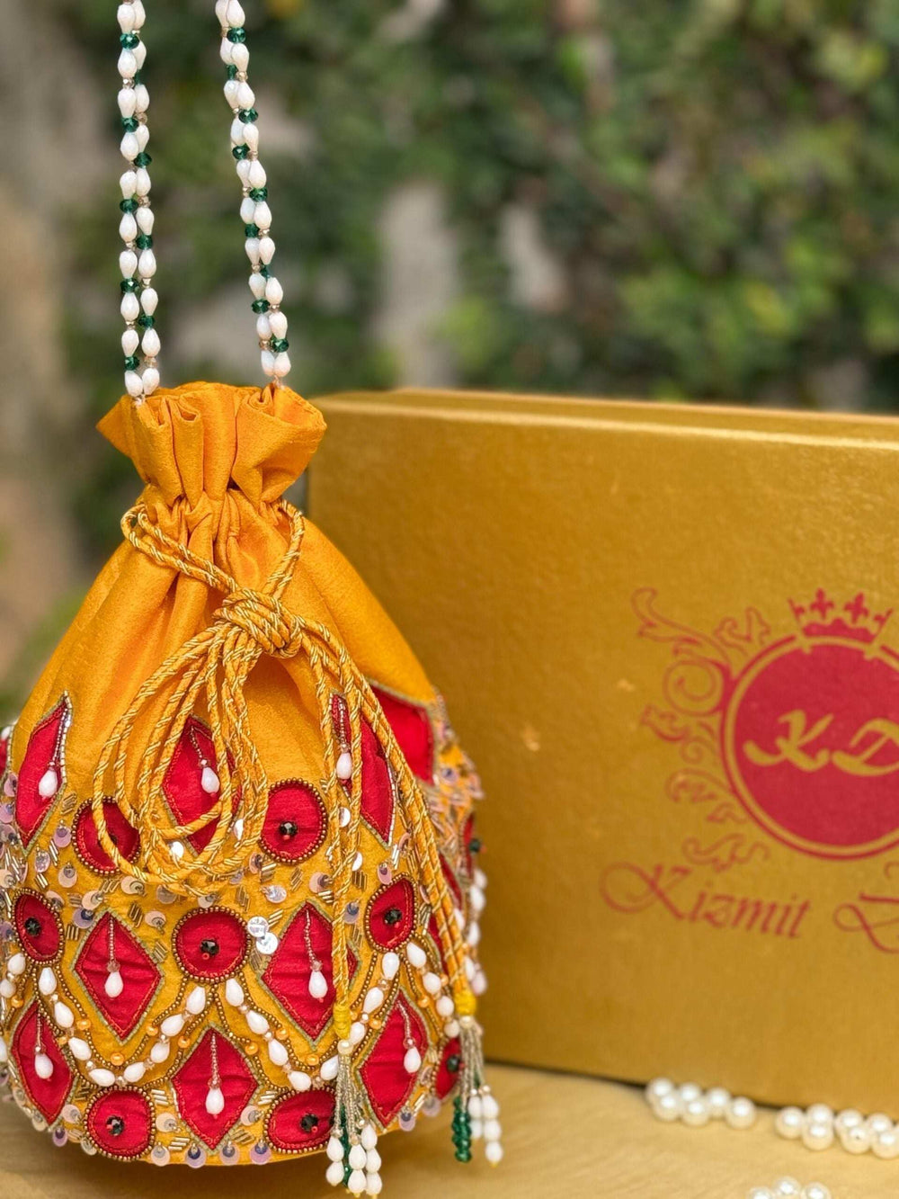 Chrome yellow potli with red patchwork and a pearl bead handle, gift box behind