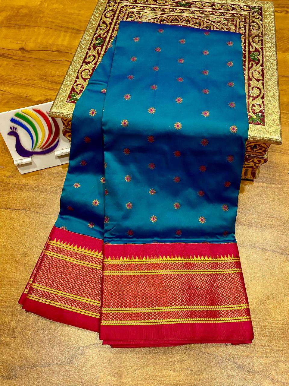 Blue Raksha kadiyal Paithani folded on a wooden table, red border with temple-tip edging