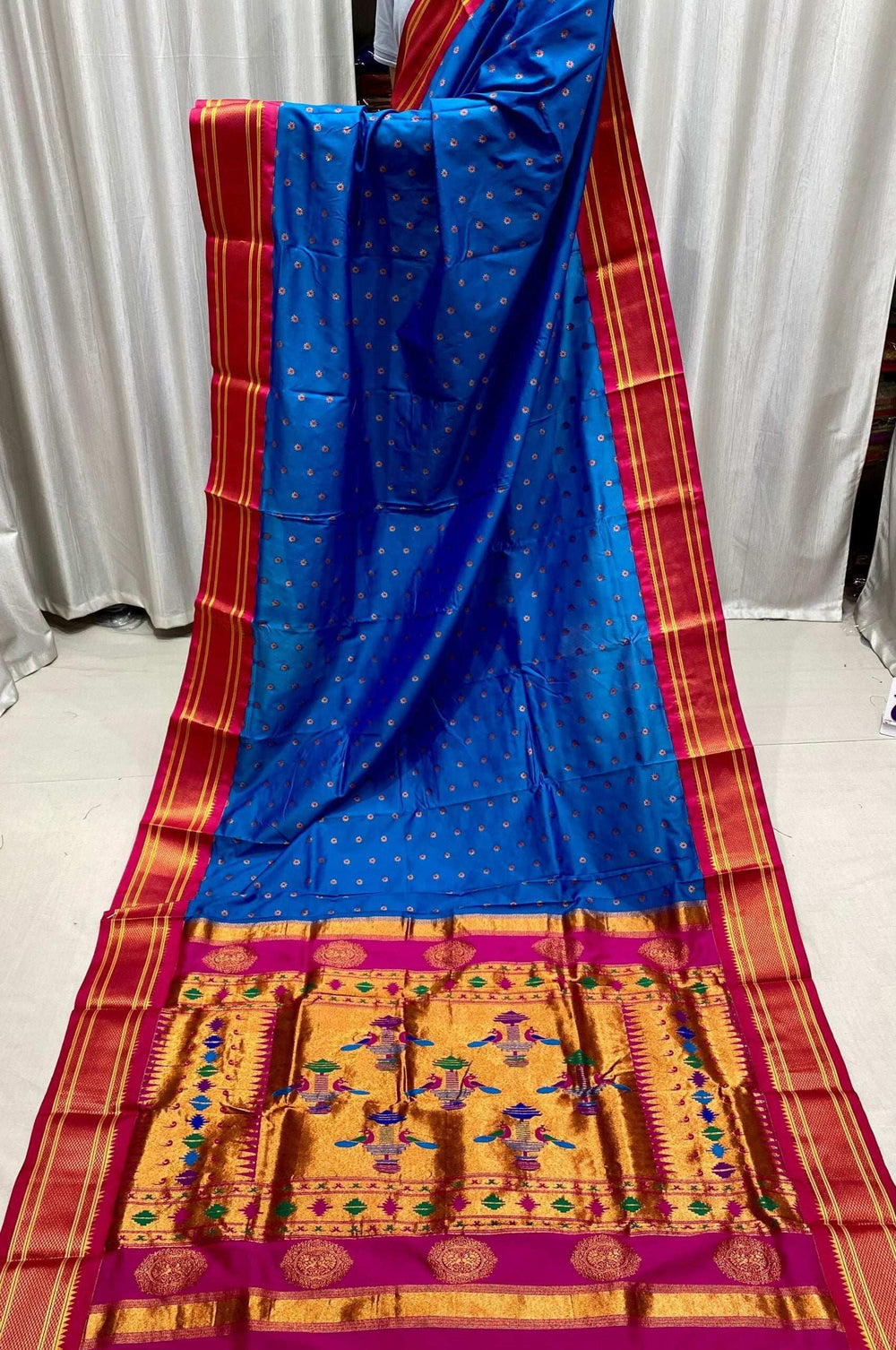 Blue saree in full drape, magenta-red kadiyal border and gold motif pallu