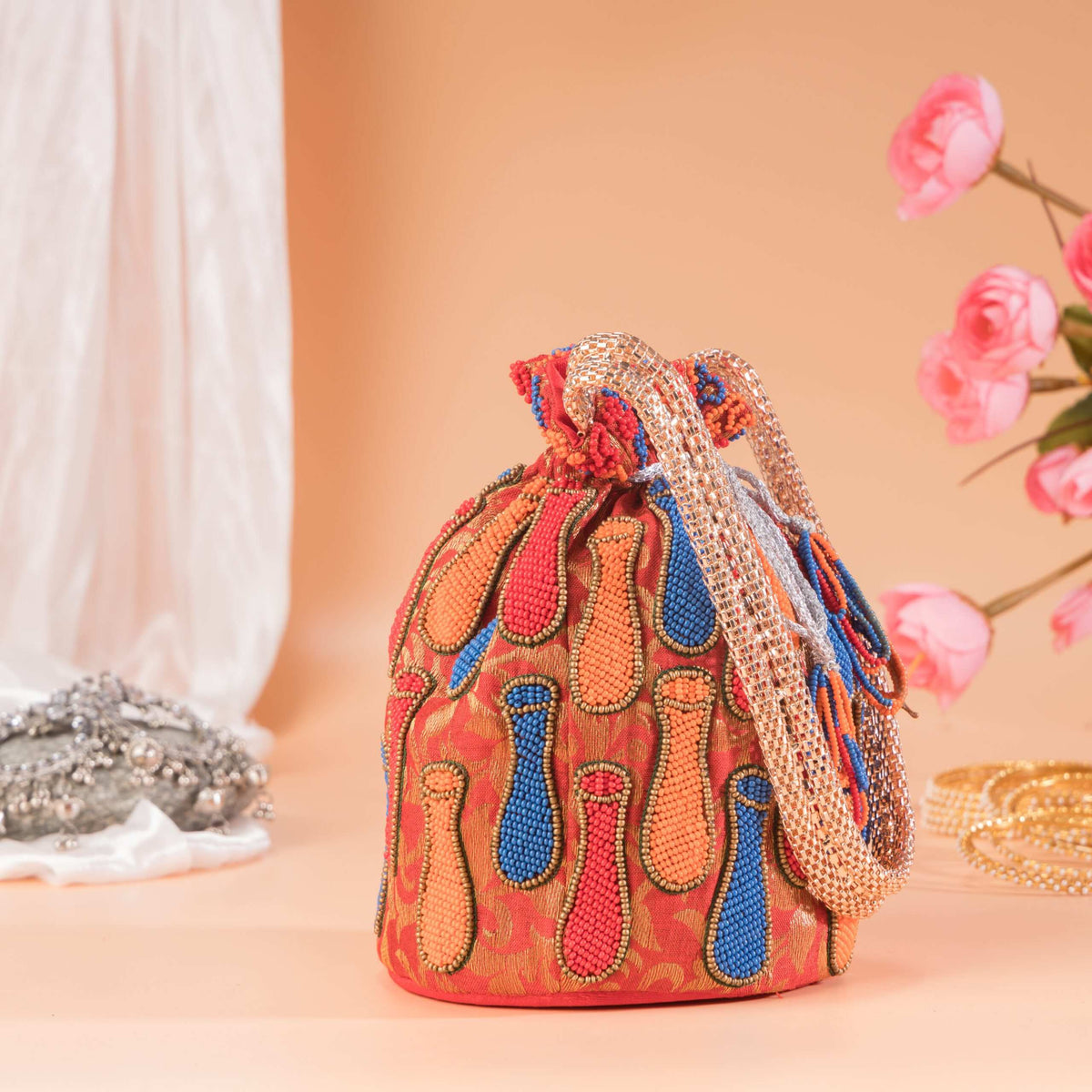 Orange brocade potli with beaded surai motifs and a gold braided handle