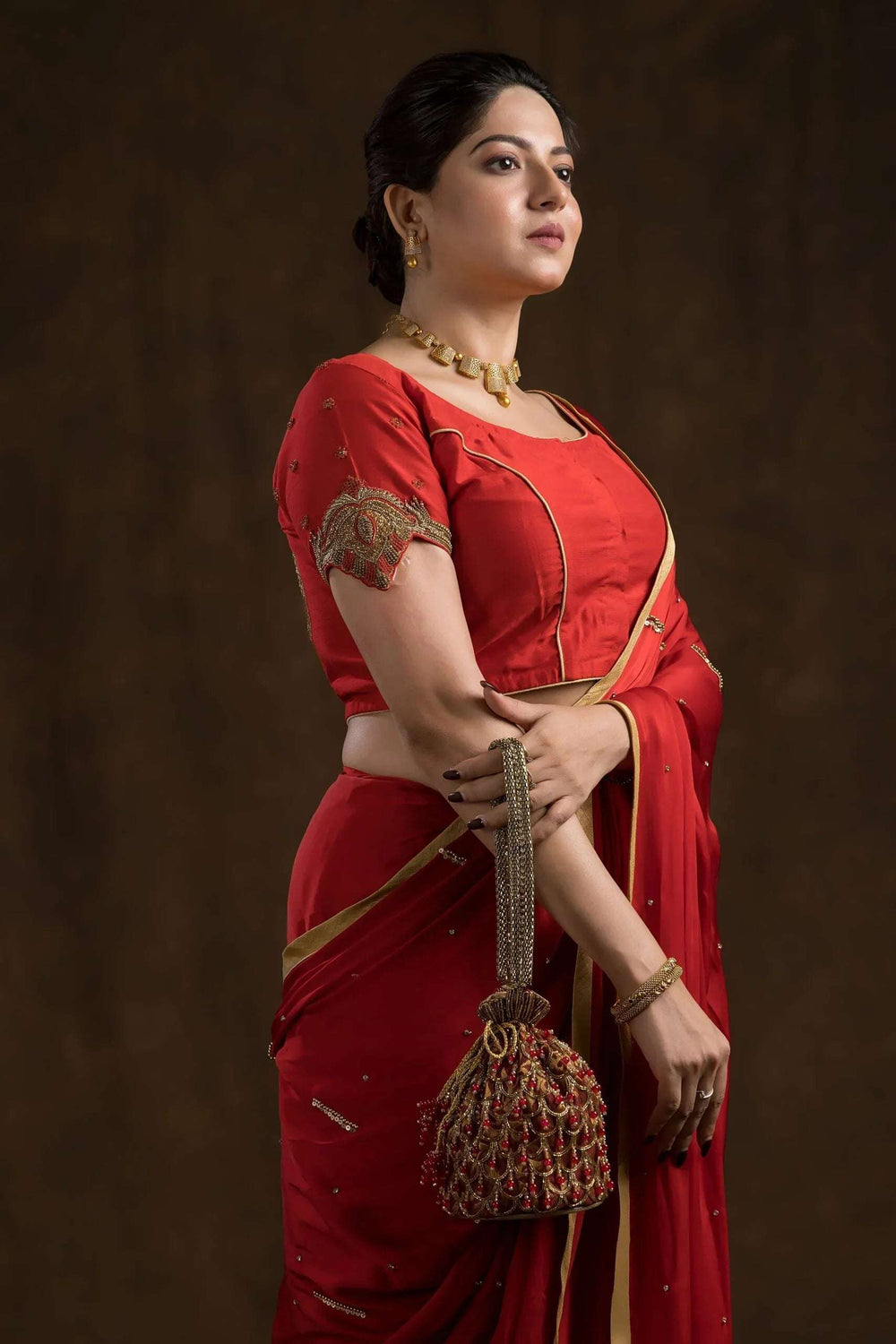 Side view showing the embroidered sleeve edge of the red blouse and potli in hand