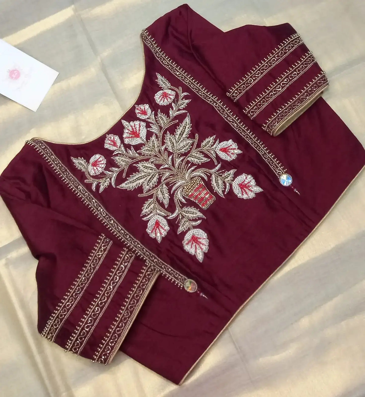 Wine-red blouse laid flat on cream fabric, gold and white floral embroidery across the back