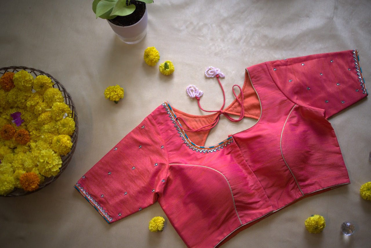 Pink blouse back flat-laid with its dori tied, marigolds and a potted plant alongside