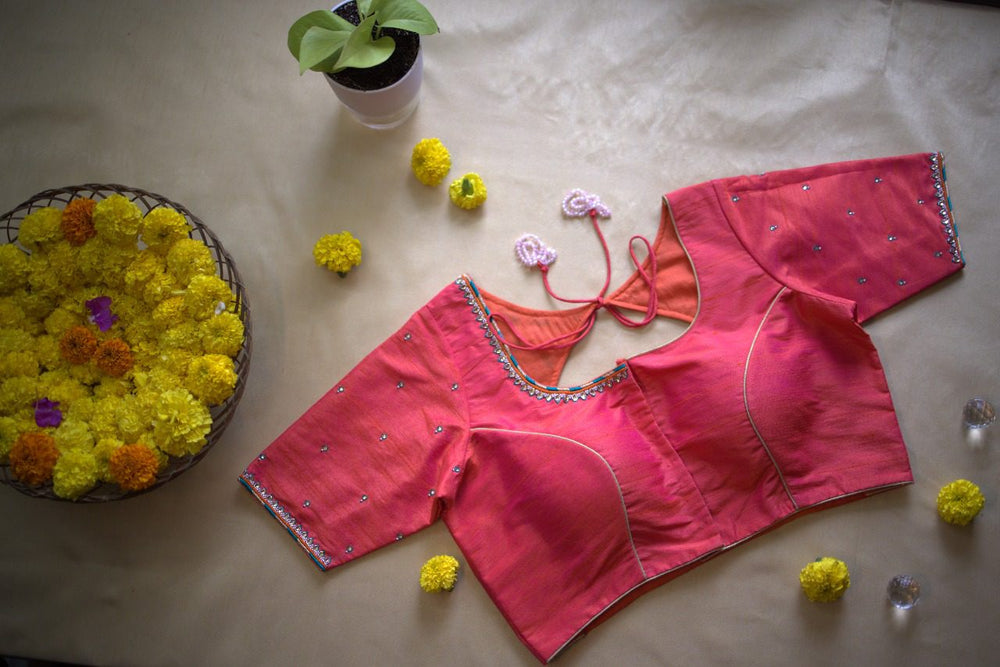 Whole blouse laid out on a beige sheet beside a basket of marigolds, back facing up