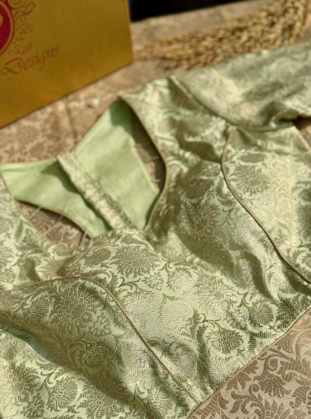 Pistachio green brocade blouse folded flat, sleeve and gold piping seen up close