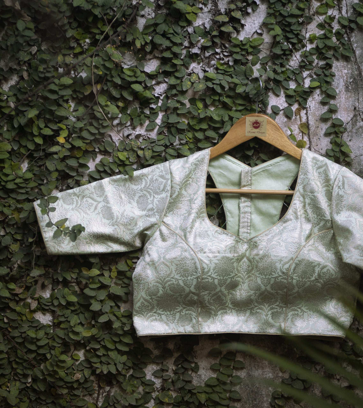 Full view of the green brocade blouse hung against an ivy-covered wall