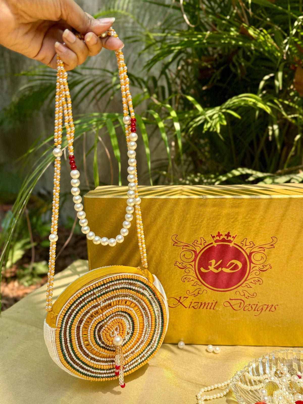 Round beaded bag held up by its pearl and gold sling chain over a Kizmit gift box