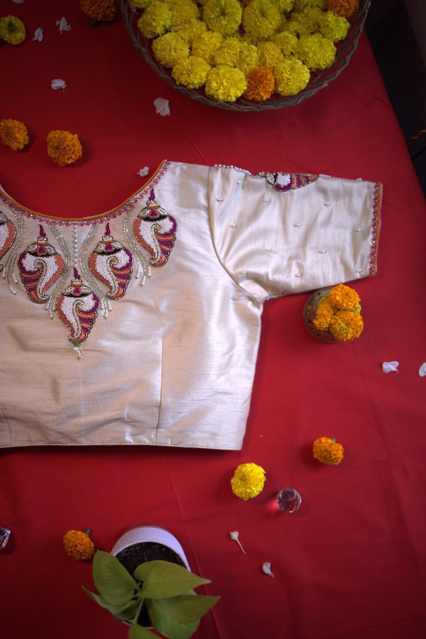 Cream blouse flat-laid on red cloth with marigolds, embroidered neck and pearl-dotted sleeves