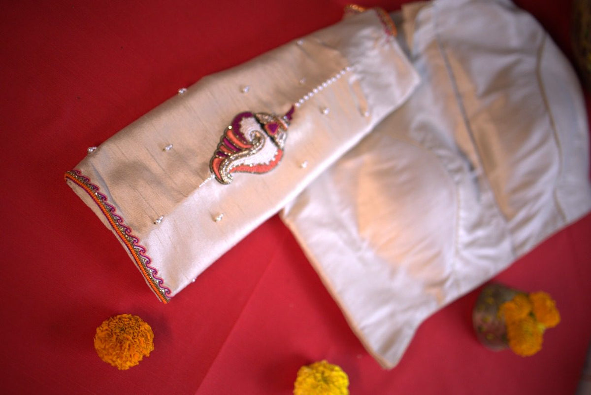 Sleeve detail with a single embroidered conch motif and scattered pearl dots