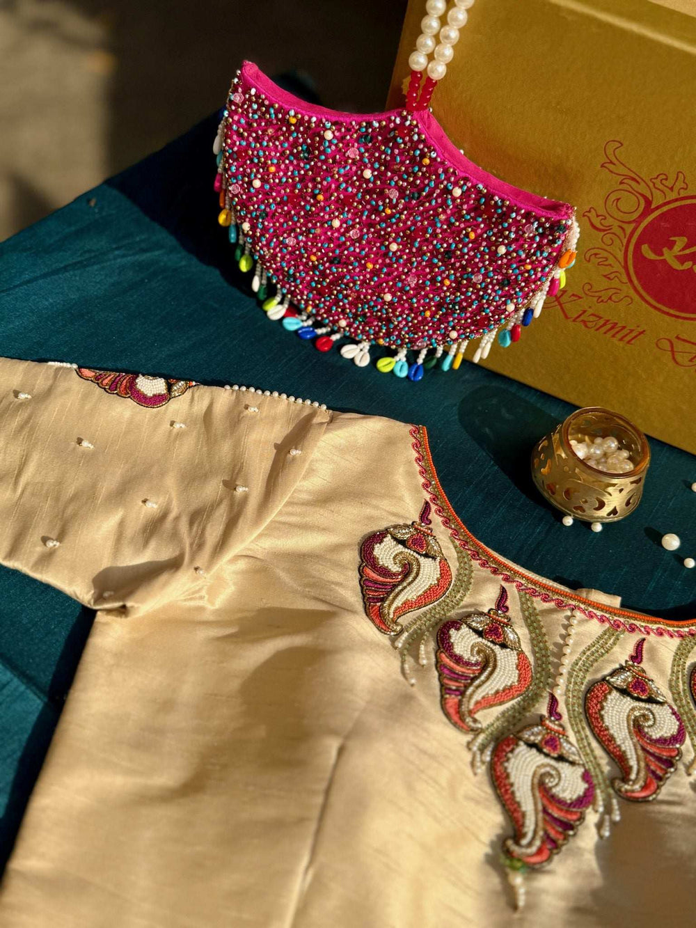 Cream embroidered blouse styled flat with a pink beaded clutch on a teal cloth
