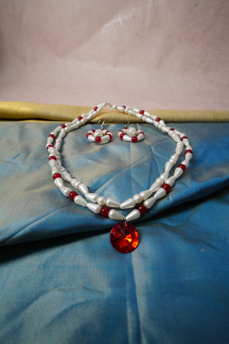 Double-strand pearl necklace with red beads and a round red pendant on blue satin