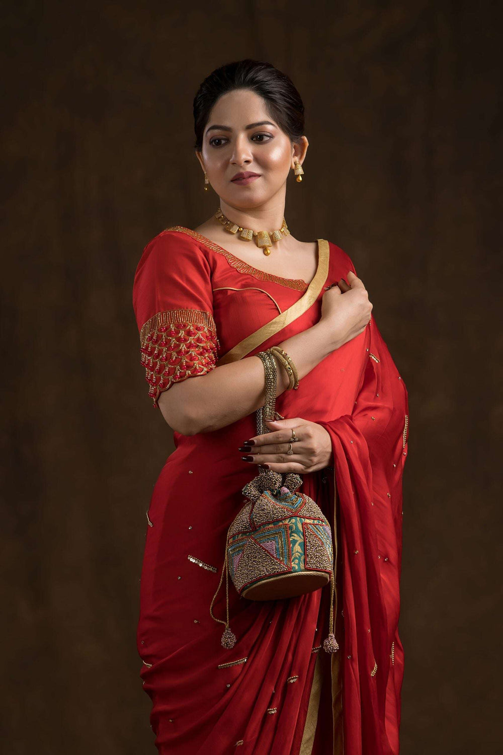 Model in a red saree holding the beaded potli bag by its gold chain handle