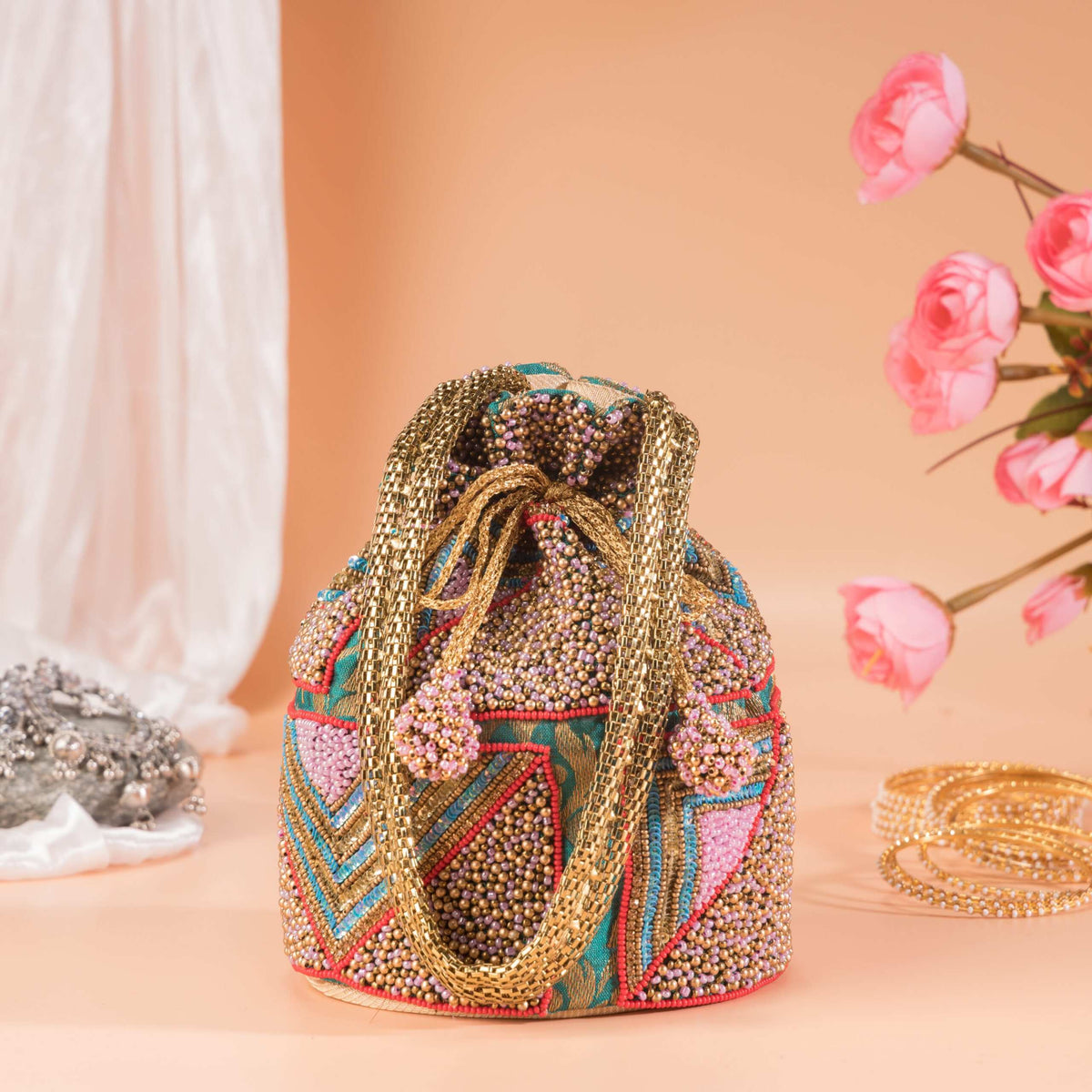Potli styled on a peach backdrop with pink roses, chain handle coiled over the drawstring