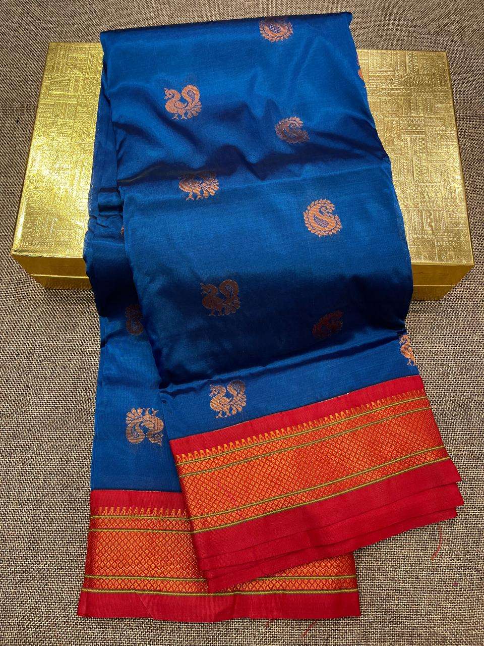 Royal blue saree body scattered with copper peacock bootis, red contrast border