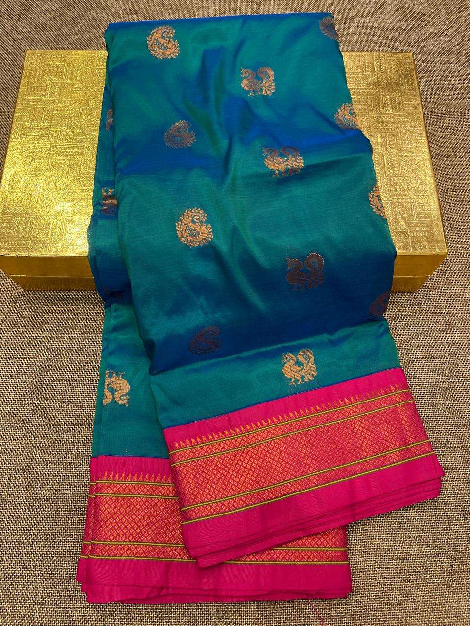 Teal green-blue saree folded to show copper bootis and rani pink brocade border
