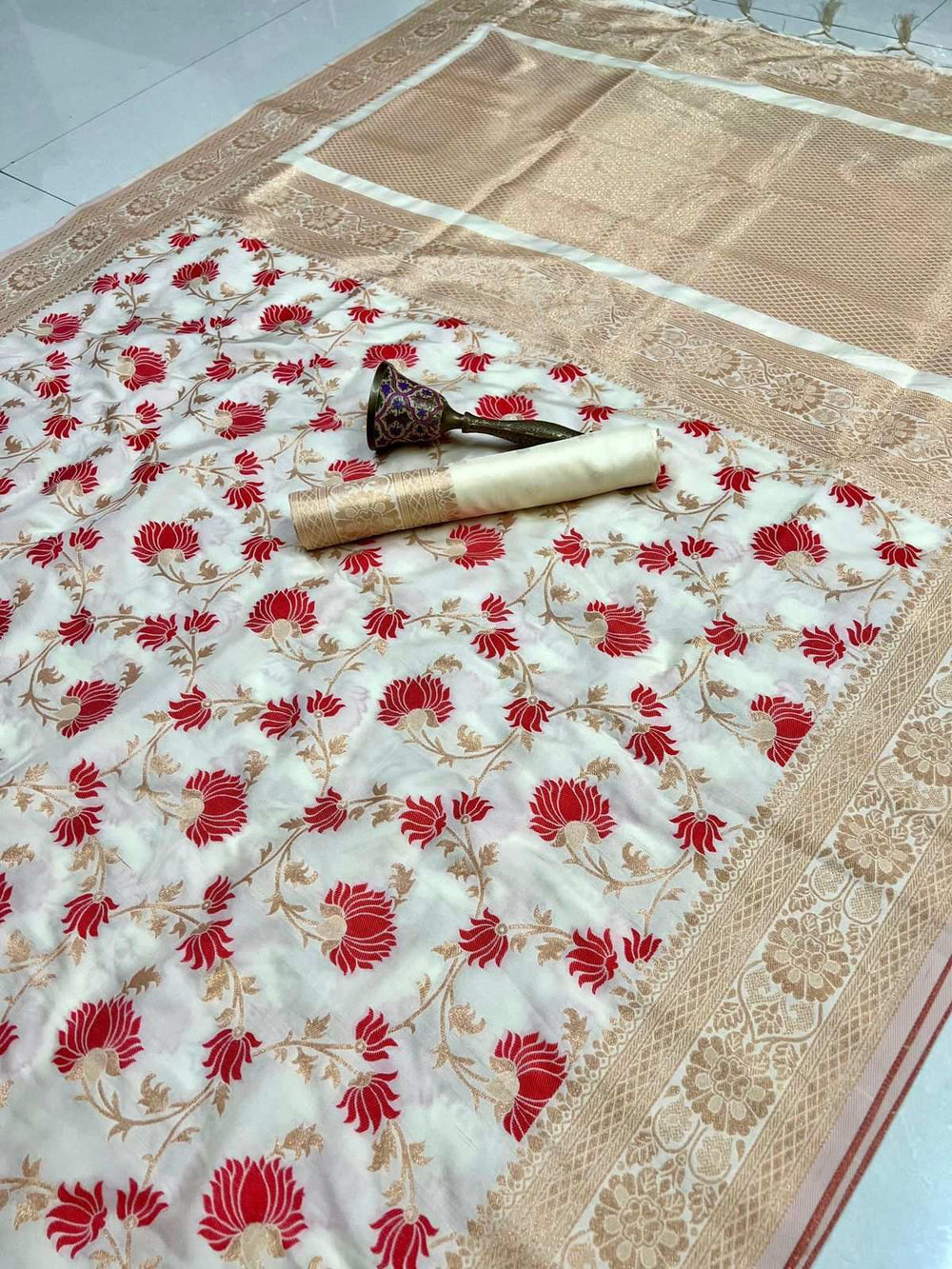 Off-white saree with red lotus flowers and gold zari border, blouse piece rolled on top