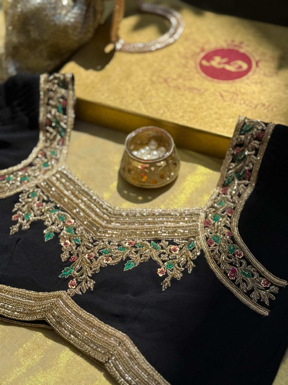 Neckline embroidery lit warmly against the gold packaging box and beaded necklace