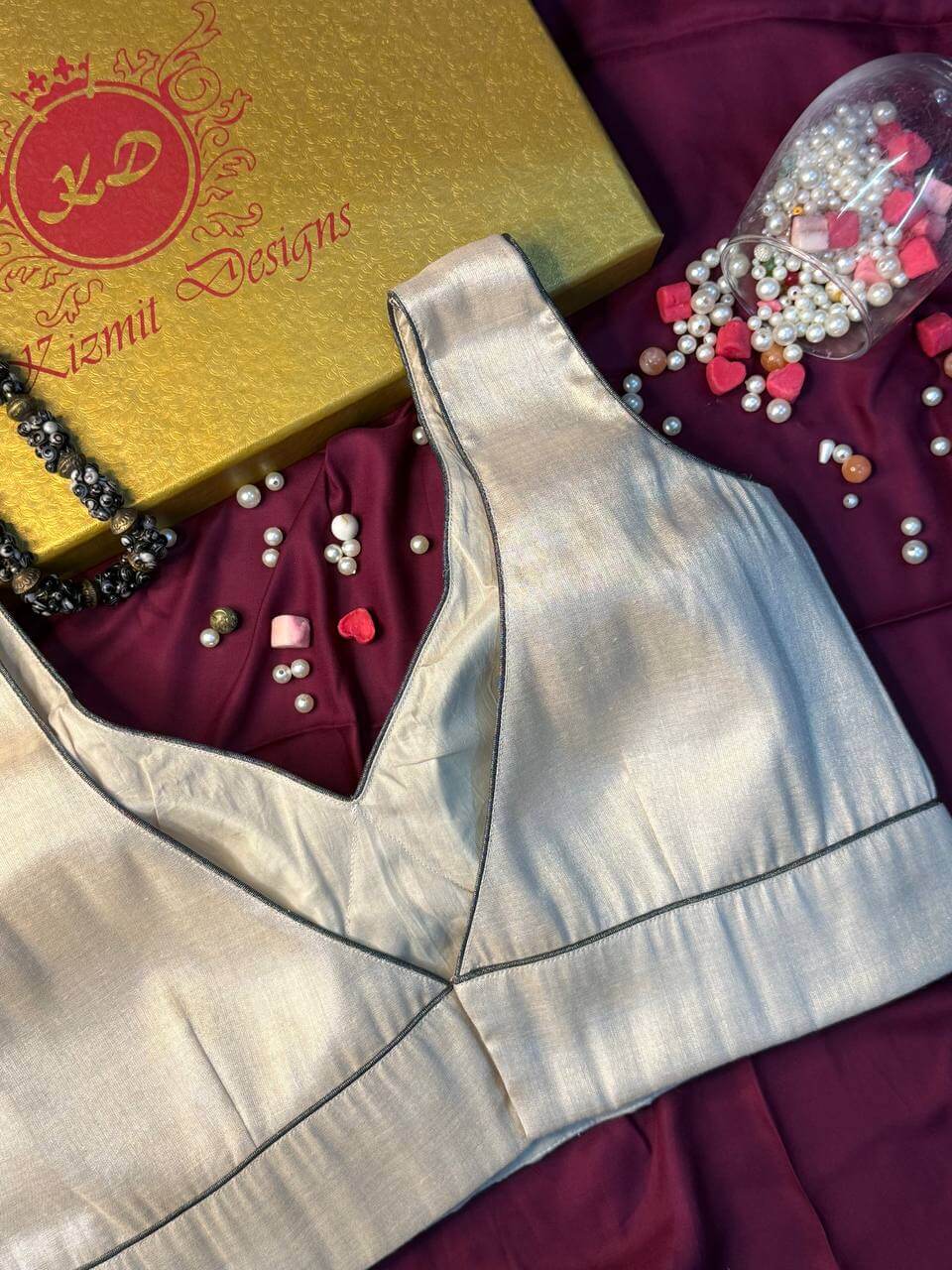 Silver-ivory blouse flat-lay on maroon fabric beside the Kizmit Designs gift box