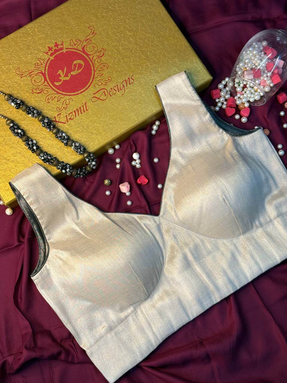 Sleeveless blouse angled on maroon fabric, piped armhole and gold box behind