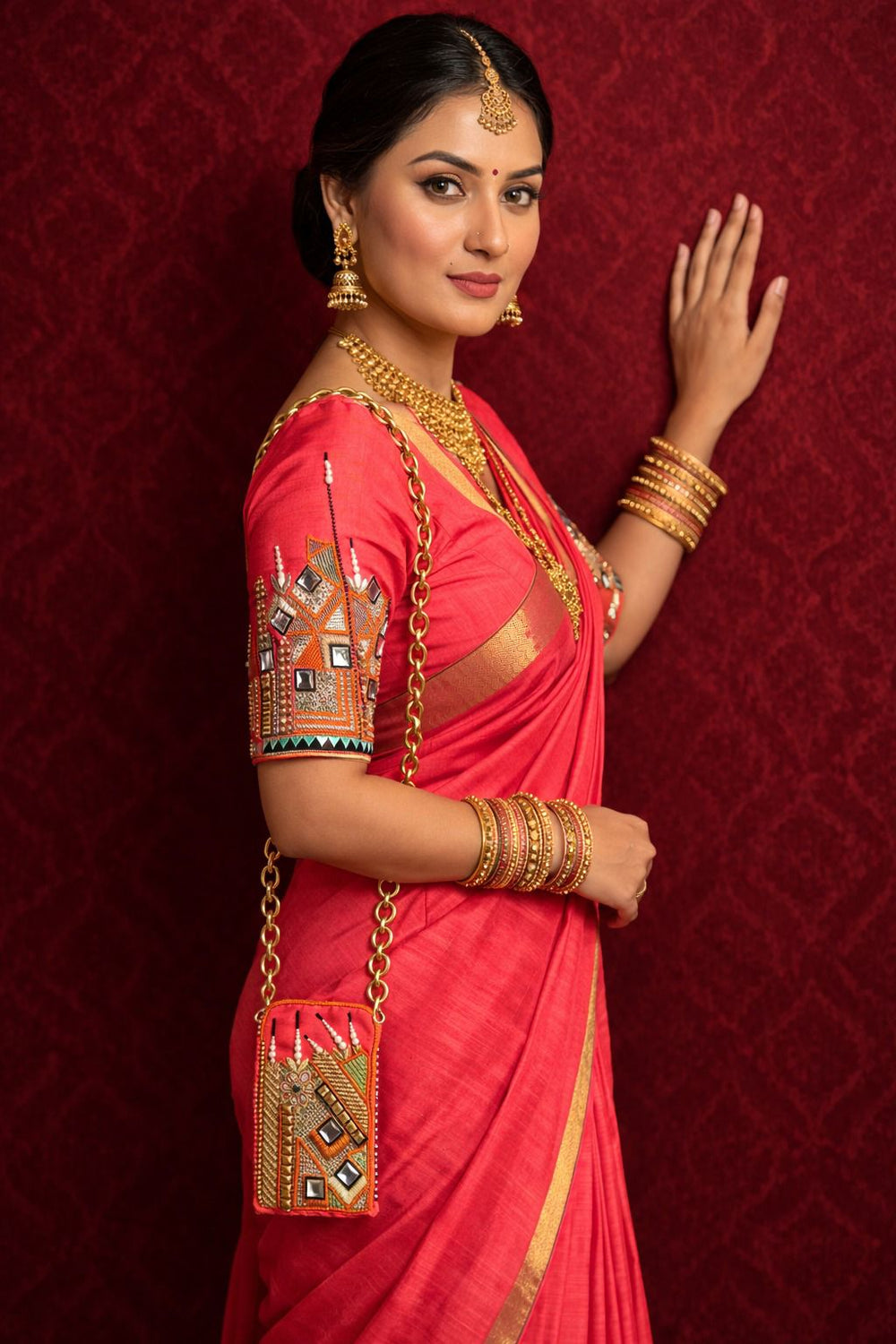 Model in a coral-pink saree with mirror-work sleeve embroidery, small chain sling bag at her hip